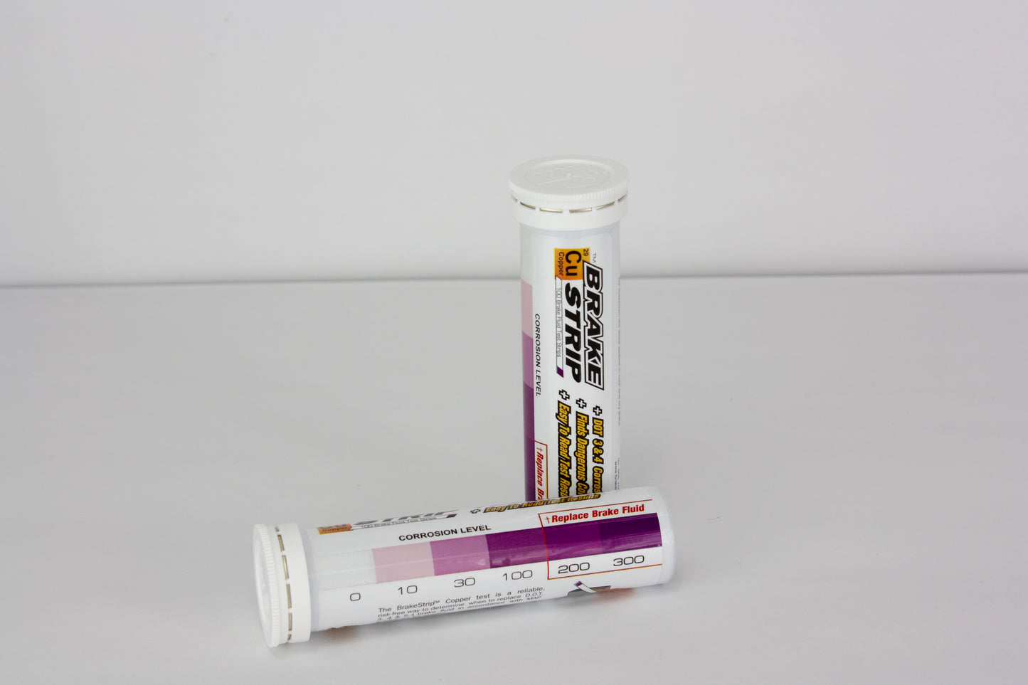 The image shows two tubes of Brake Fluid Test Strips sitting on a table. The text on the tubes is appears to be a label for the product and instructions on how to use the test strips. There is also a chart that indicates a range of corrosion levels.