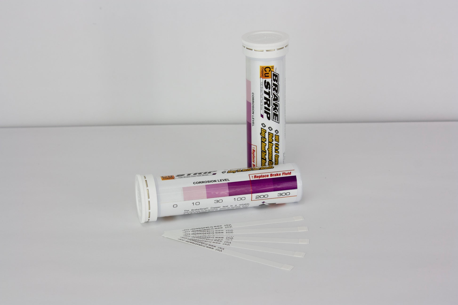 The image shows two tubes of Brake Fluid Test Strips sitting on a table. The text on the tubes is appears to be a label for the product and instructions on how to use the test strips. There is also a chart that indicates a range of corrosion levels.